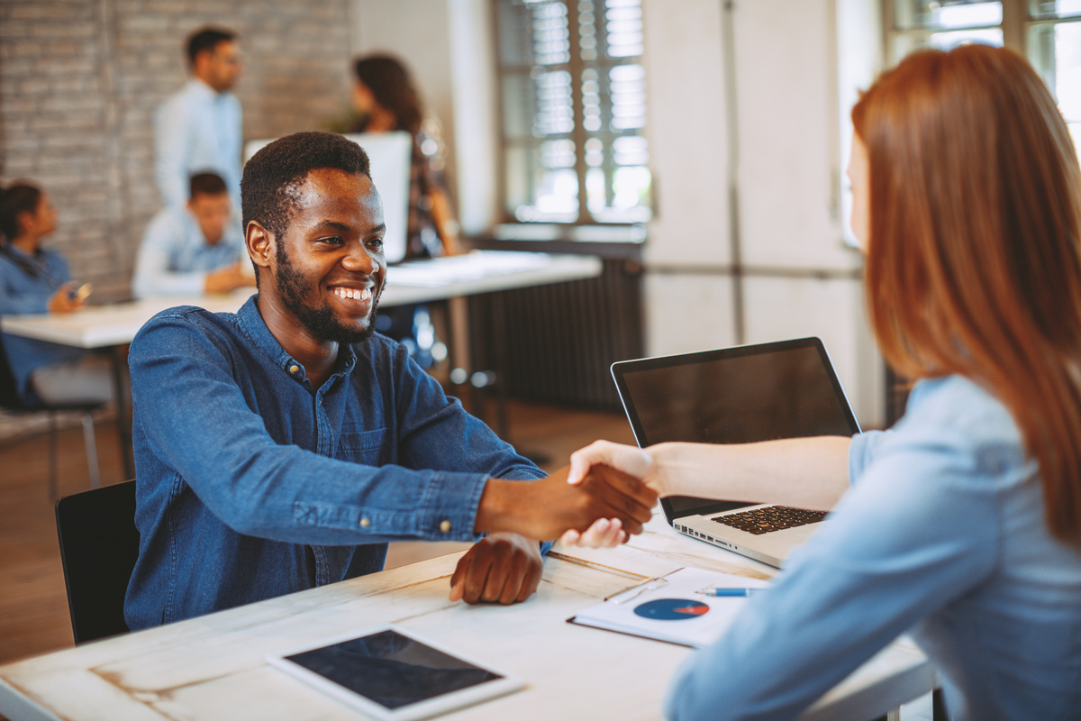 Homem sorrindo enquanto aperta as mãos de contratadora durante sua entrevista de emprego.