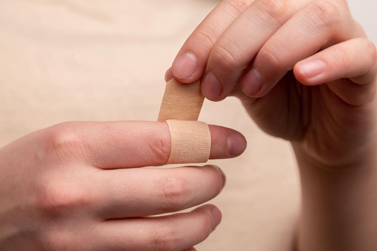 Pessoa colocando bandaid em dedo machucado, cortado