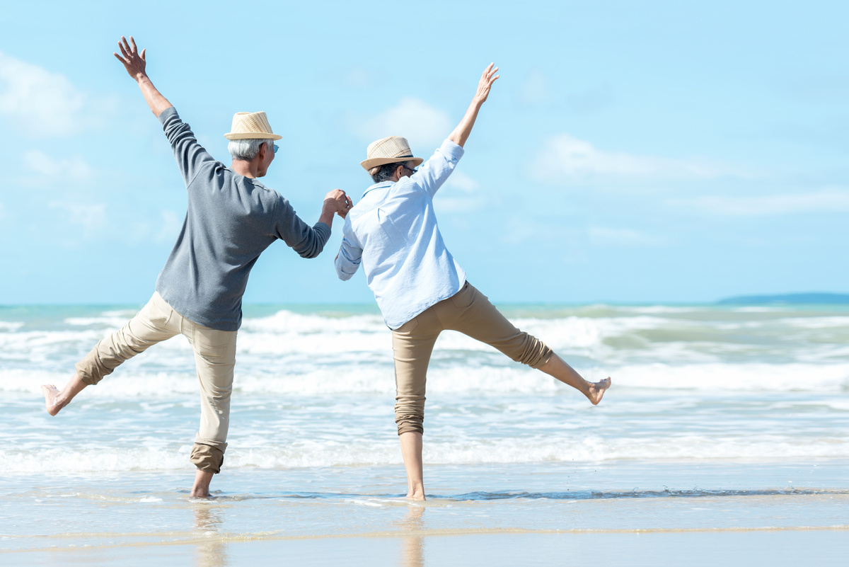 Casal na praia de mãos dadas em frente ao mar.