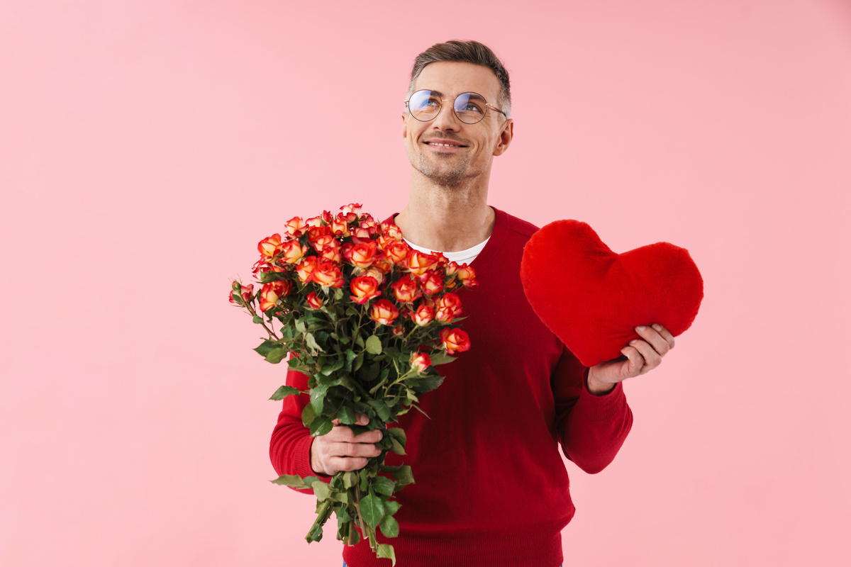 Homem segurando buquê de flores e uma pelúcia de coração, simbolizando a sensibilidade do homem de Peixes.