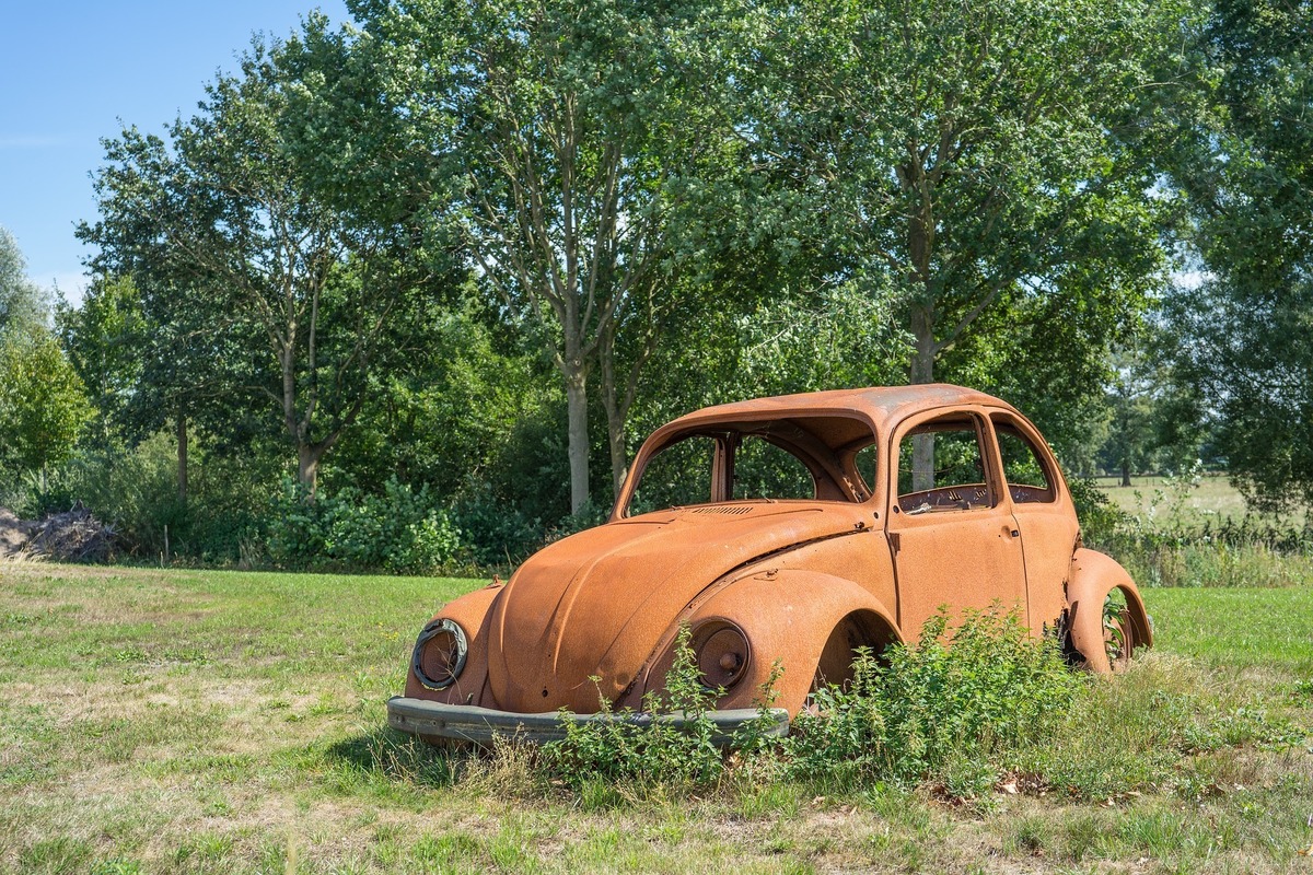 Fusca velho e enferrujado, abandonado em campo com árvores e arbustos.