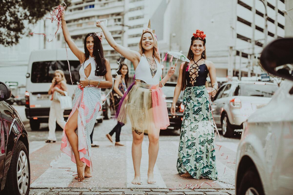 Três mulheres fantasiadas pulando carnaval. 