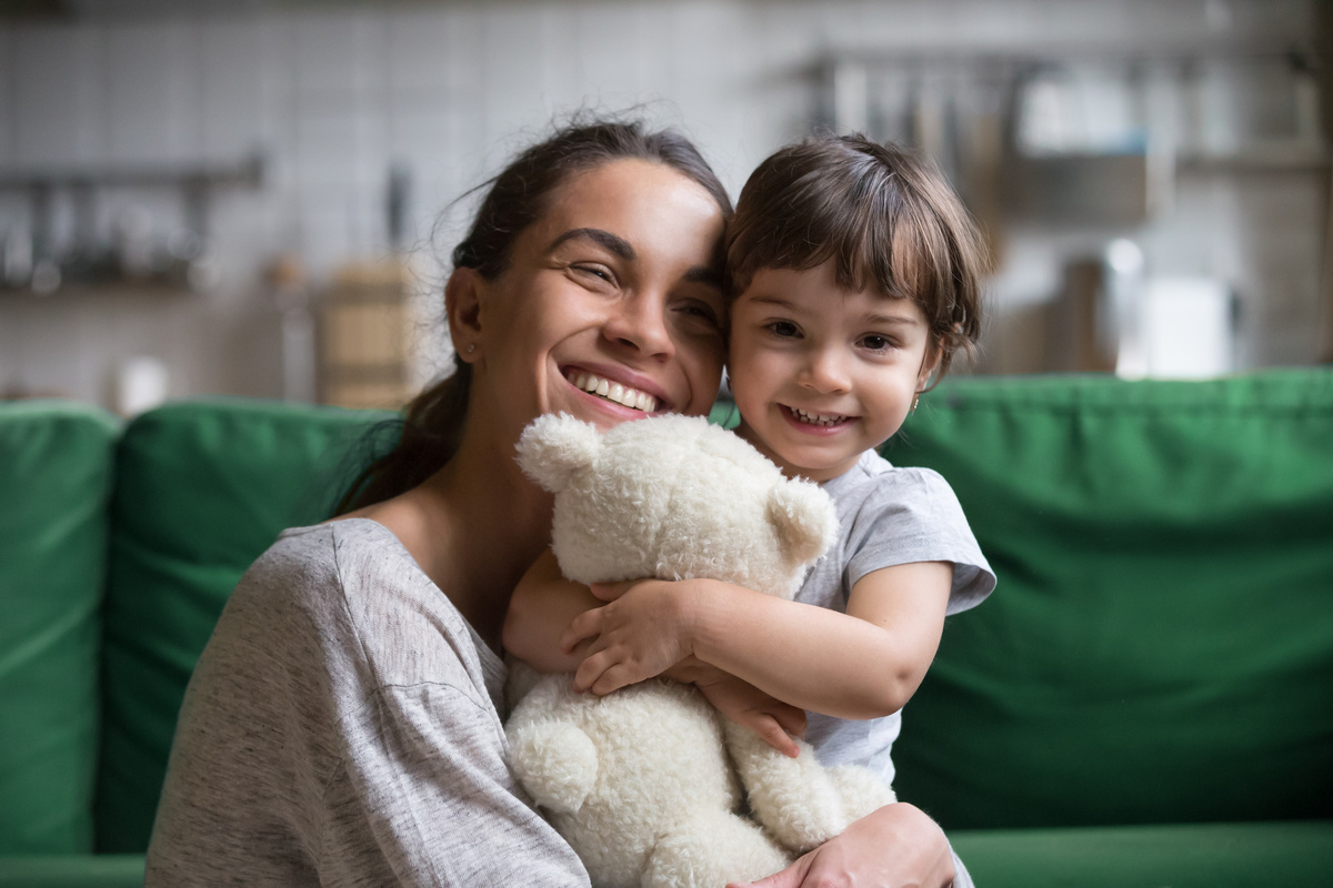 Mãe com filha adotiva sentadas no sofá rindo.