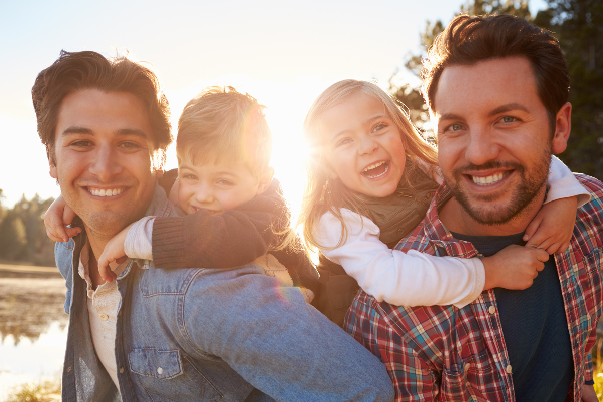 Casal gay com filhos adotivos no colo.