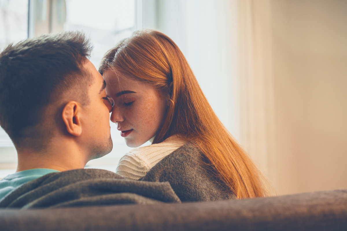 Casal com rostos próximos sentados em sofá