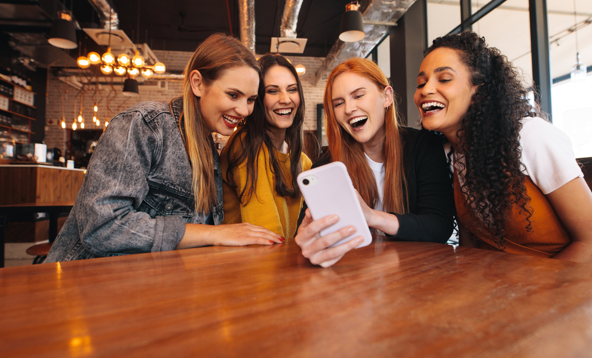 Grupo de amigas rindo enquanto tiram foto em celular. 