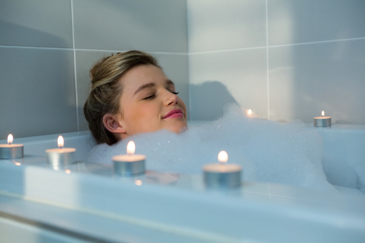 Mulher relaxando em banheira com espuma alta e velas em volta. 