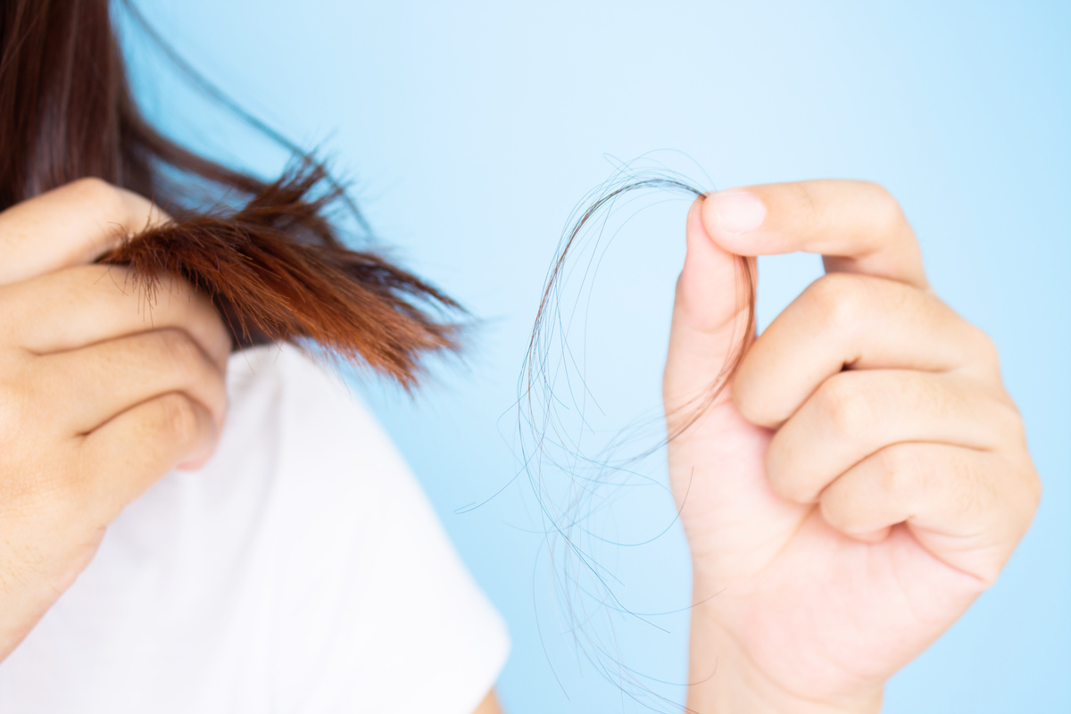 Pessoa segurando cabelo que caiu, enquanto também segura as mechas de seu cabelo castanho.