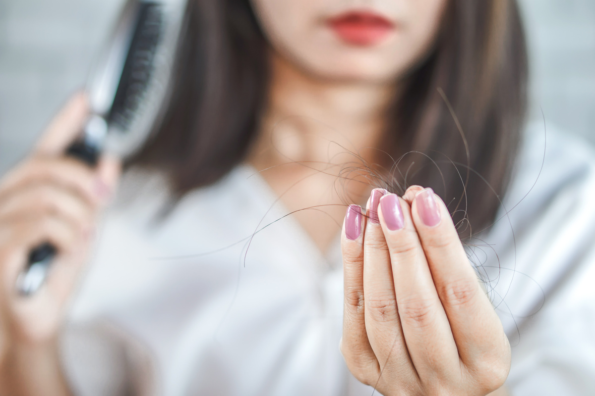 Mulher com unhas pintadas de rosa segurando tufos de cabelo que caiu enquanto ela penteava os cabelos.