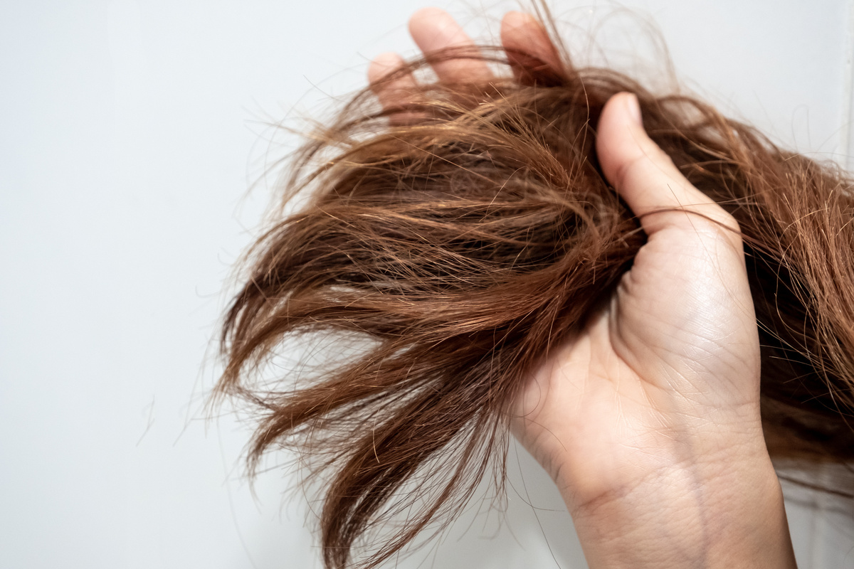 Mão segurando mechas grossas de cabelo castanho-claro.