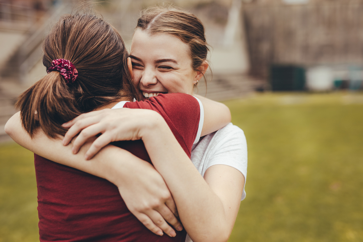 Duas amigas se abraçando, enquanto uma sorri, representando a dedicação de Escorpião nos relacionamentos.