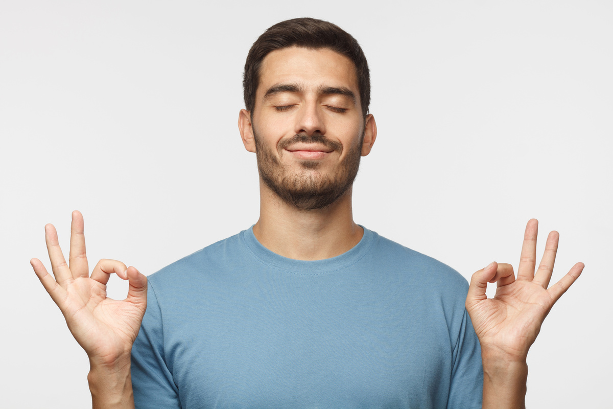 Homem fazendo sinais de meditação com as duas mãos enquanto tem os olhos fechados e um semblante calmo, representando a tranquilidade do homem de Libra.