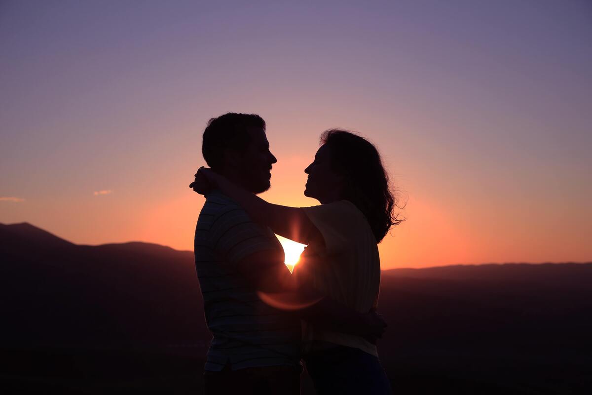 Silhueta de casal abraçado ao pôr do sol.