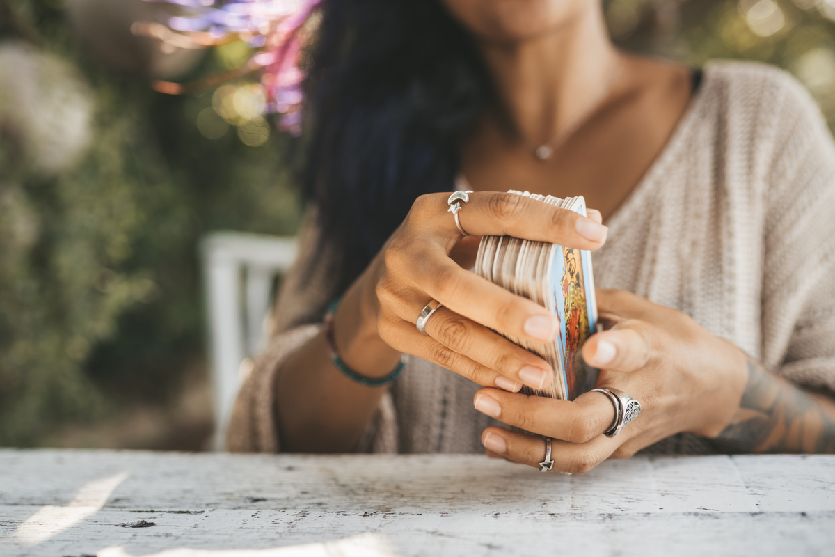 Mulher com anéis nos dedos organizando baralho de tarot em um único monte.