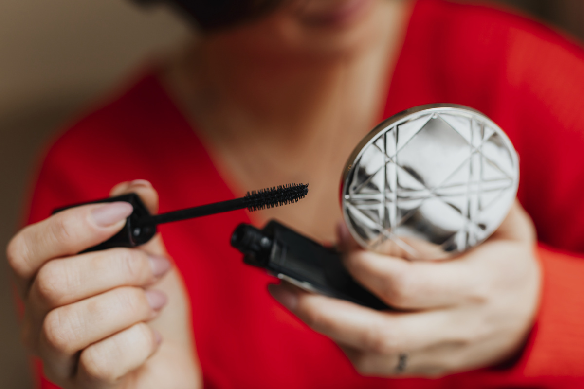 Mãos femininas segurando pequeno estojo de maquiagem e uma máscara para cílios. 