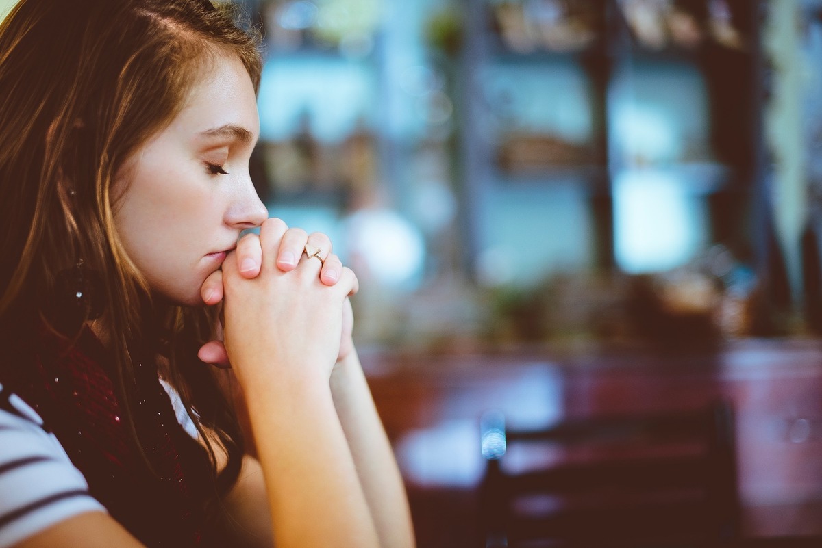 Garota com as mãos cruzadas e apoiadas no rosto, em posição de reza. 