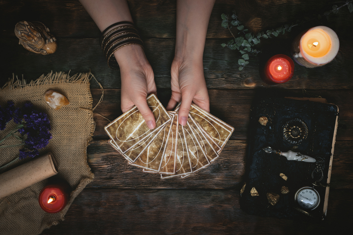 Pessoa abrindo baralho de cartas em cima de mesa de madeira, com velas e cristais ao redor.