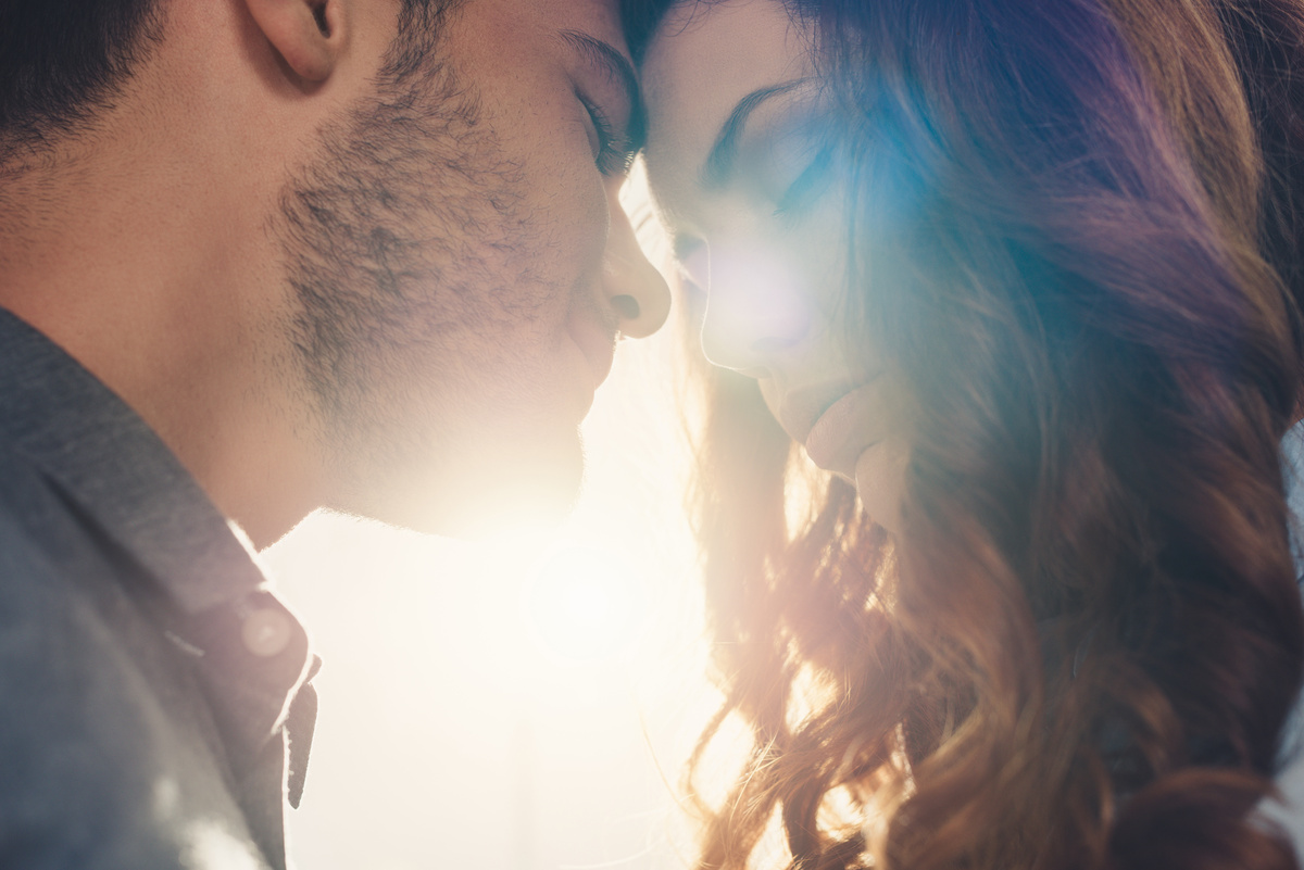 Homem e mulher encostando suas testas juntos, enquanto luz do sol passa no espaço entre eles, sendo um amor que pode ou não ter iniciado por meio de amarração amorosa.