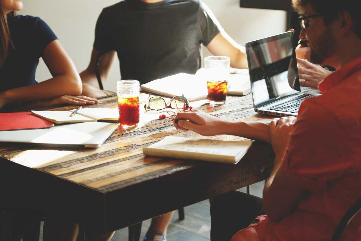 Pessoas em volta de uma mesa com cadernos, copos e um notebook.