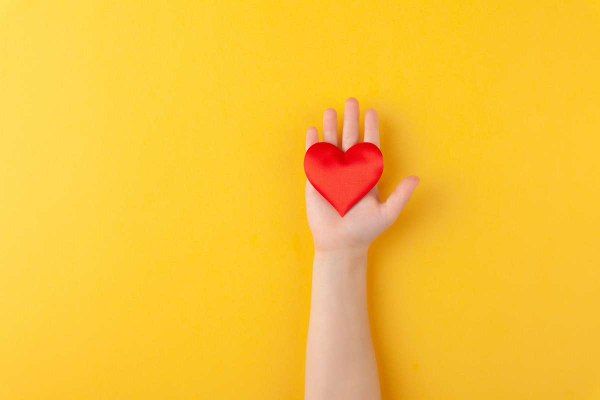 Mão segurando  coração em fundo amarelo; Vênus na casa 7 no amor