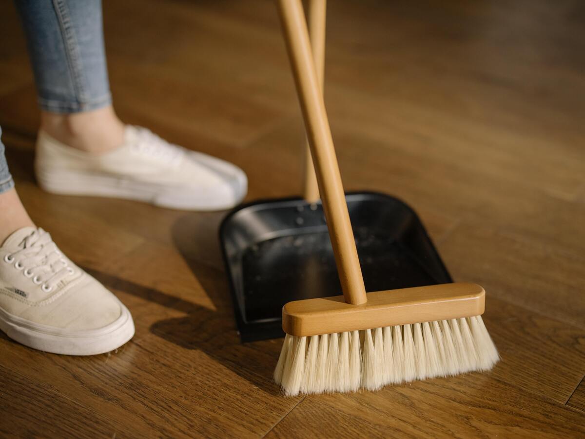 Pés de uma mulher, vassoura arrastando lixo para a pá.