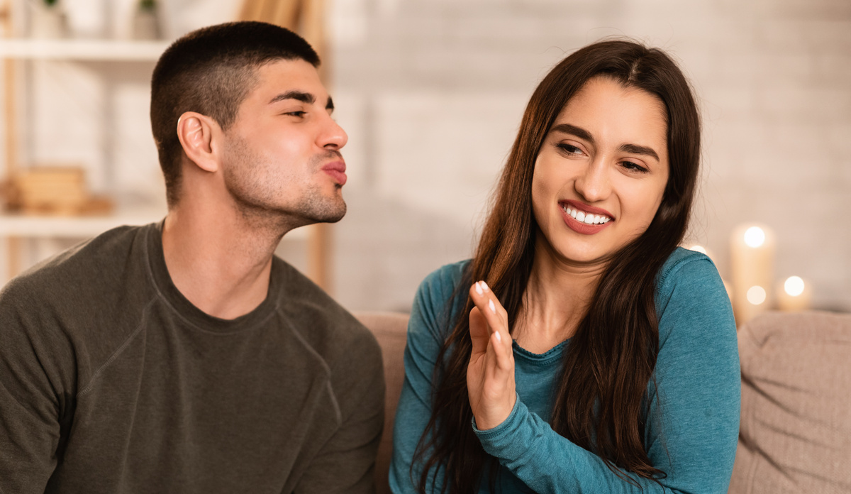 Homem tentando beijar rosto de mulher, que, com uma careta, se afasta, em sinal de rejeição.