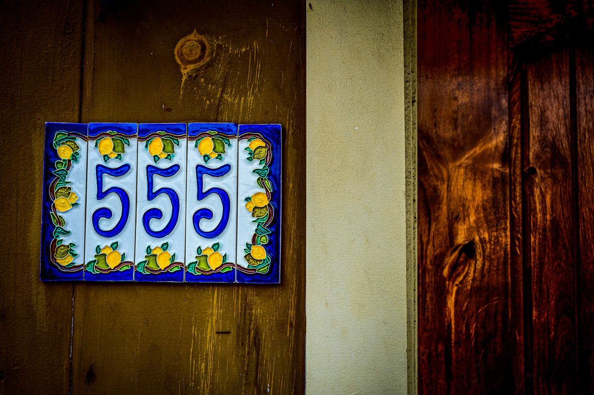 Placa branca com número 555 em azul, contornado por pequenos limões desenhados.