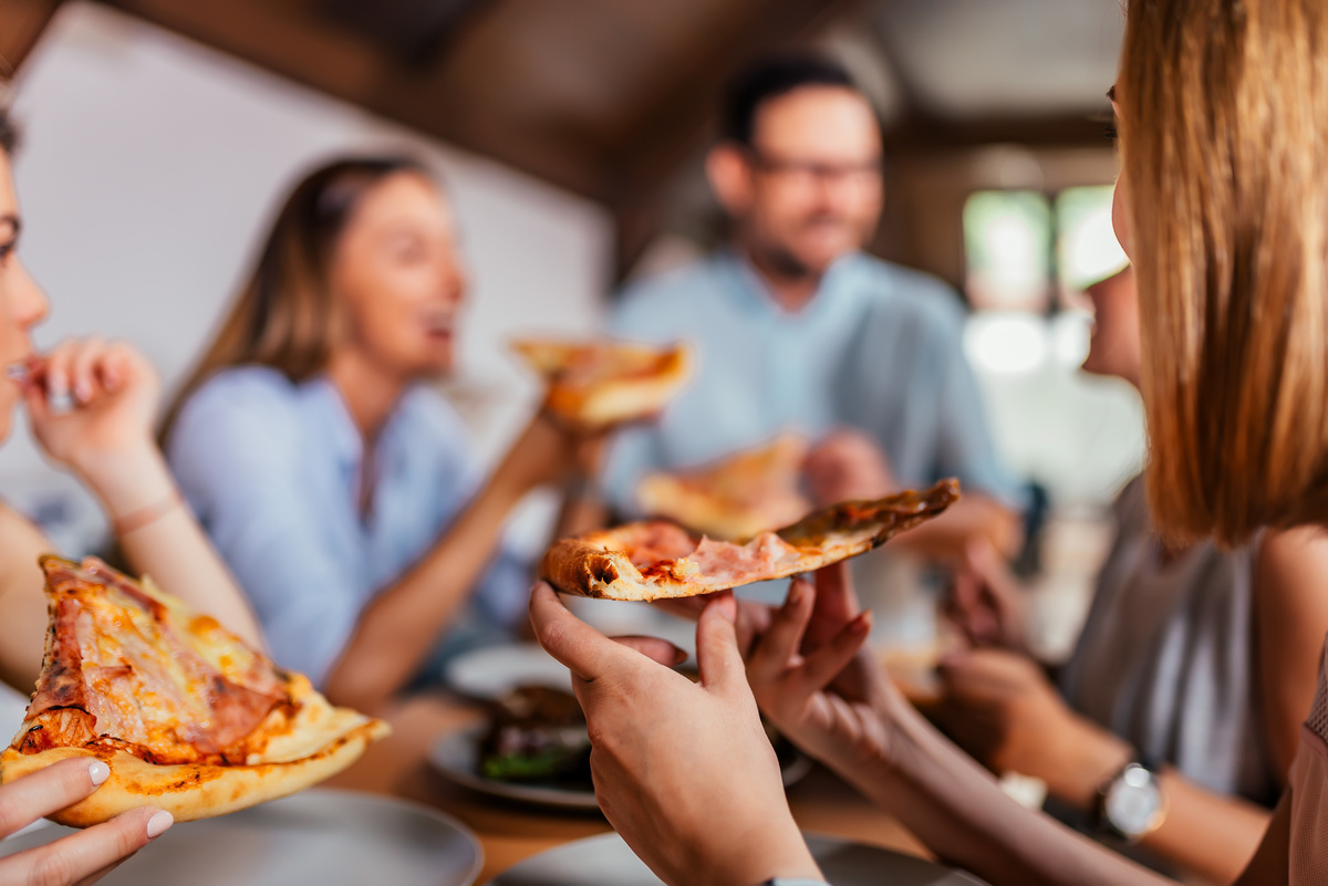 Grupo de amigos sentados à mesa e comendo pizza.