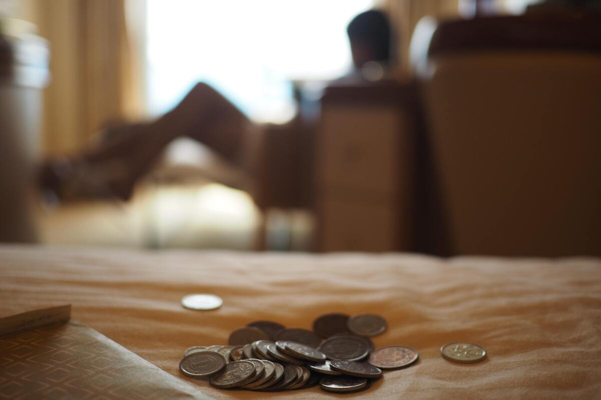 Moedas jogadas na cama e uma mulher desfocada ao fundo.