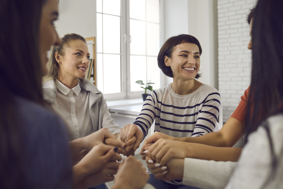 Mulher segurando mãos de todas as amigas enquanto sorri, representando o carinho de Libra em seus relacionamentos.