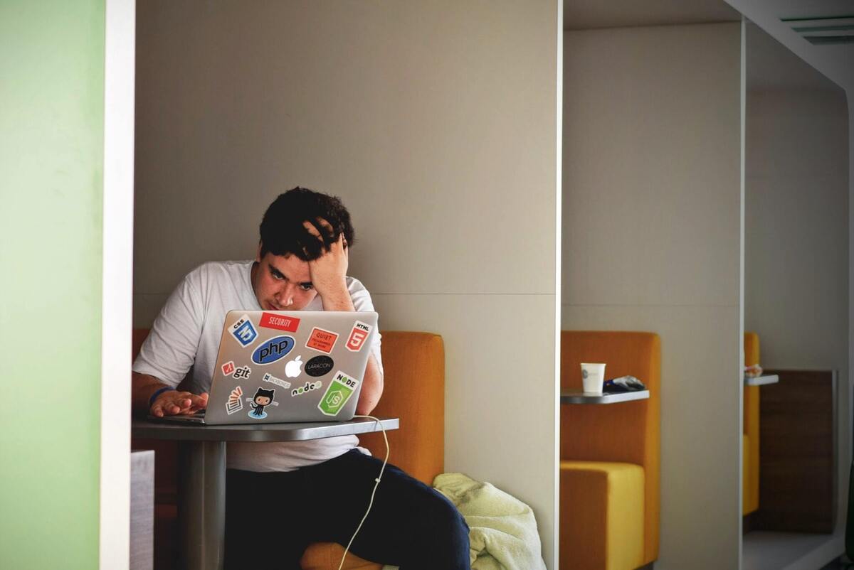 Homem sentado, olhando para o notebook com a mão na cabeça. 