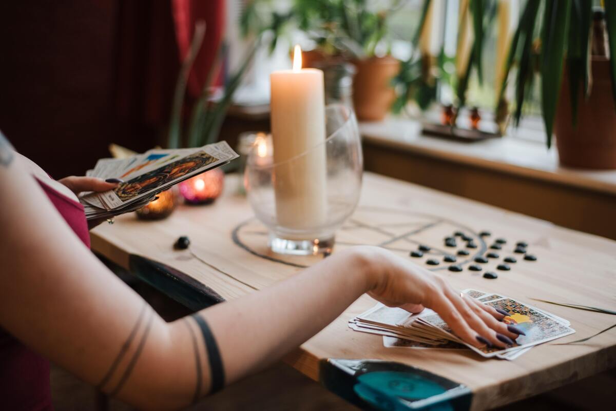 Mulher mexendo com cartas de tarô em cima da mesa.