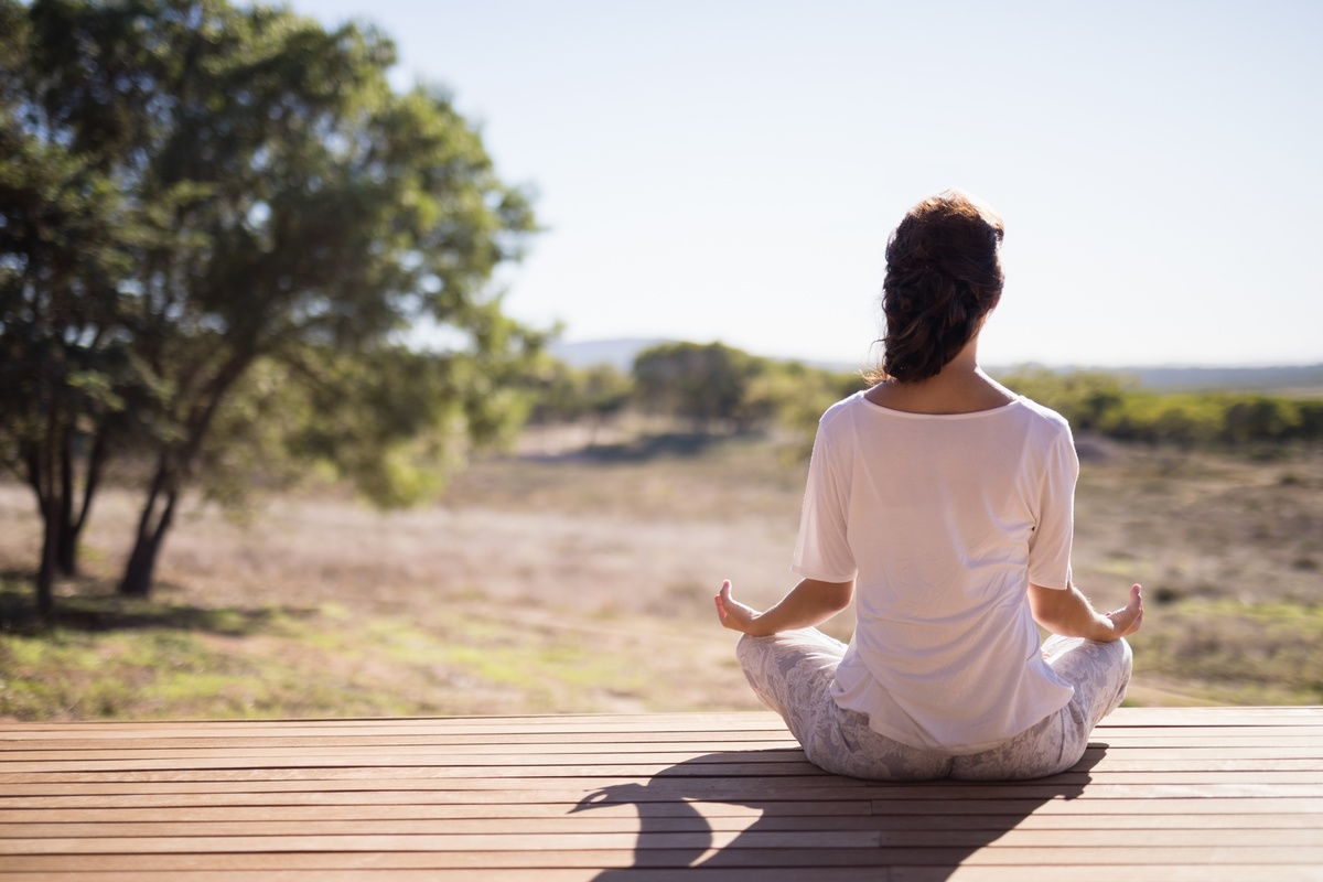 Mulher de costas enquanto faz yoga ao ar livre, sendo essa uma das práticas da Ayurveda.