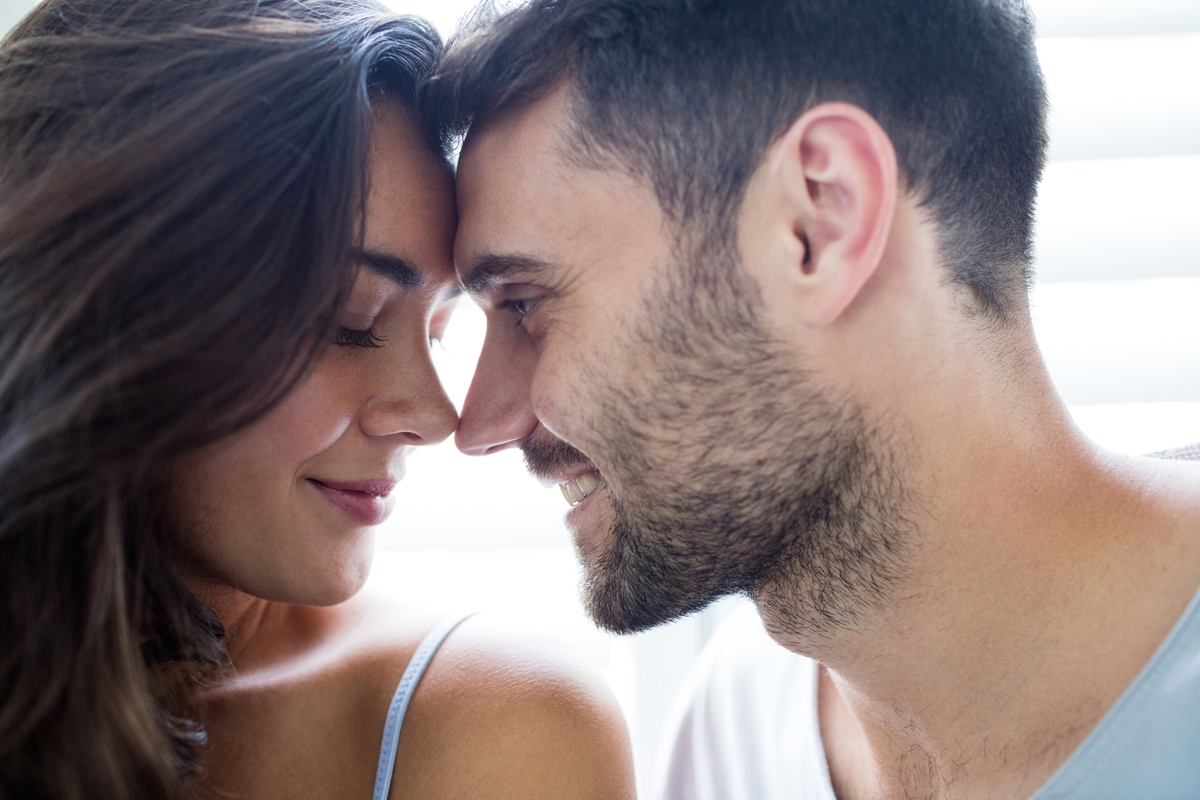 Casal de homem e mulher com os rostos próximos, enquanto homem olha para mulher, ela tem os olhos fechados, representando a intimidade de Touro e Aquário.