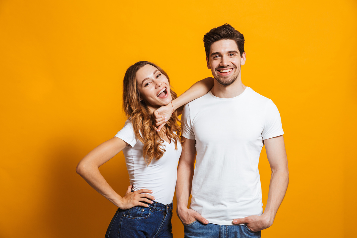 Em fundo amarelo, homem e mulher posando juntos enquanto sorriem, representando Touro e Aquário nos dois gêneros.