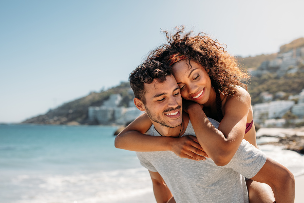 Casal de homem e mulher abraçados na praia.