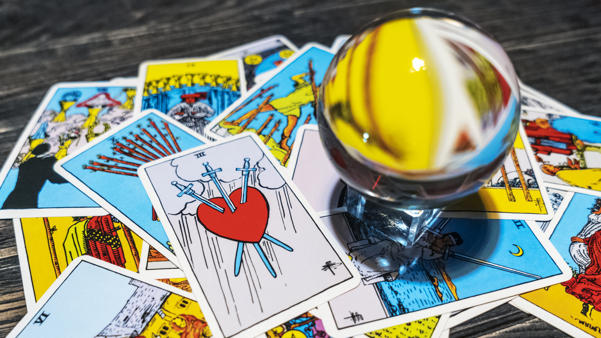 Carta 3 de Espadas do Tarot ao lado de outras cartas e bola de cristal