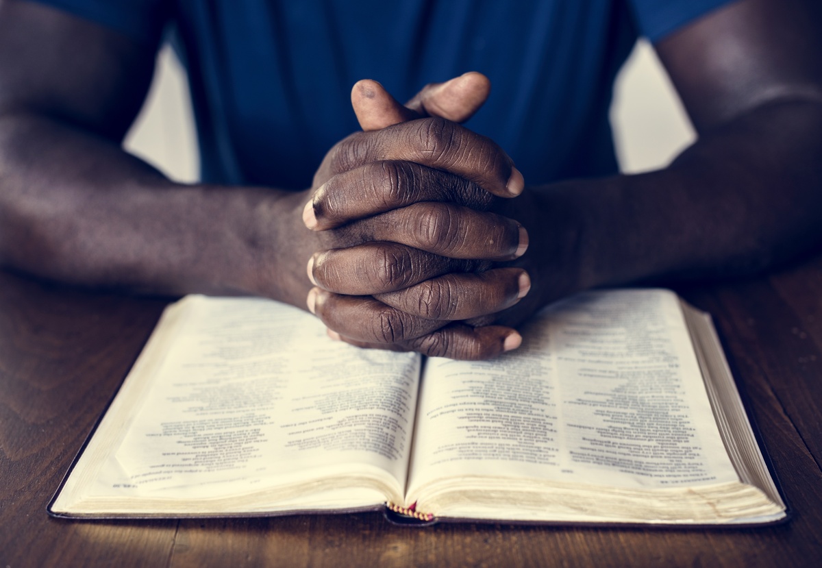 Homem com as mãos cruzadas em cima de Bíblia aberta enquanto faz a leitura de salmos.