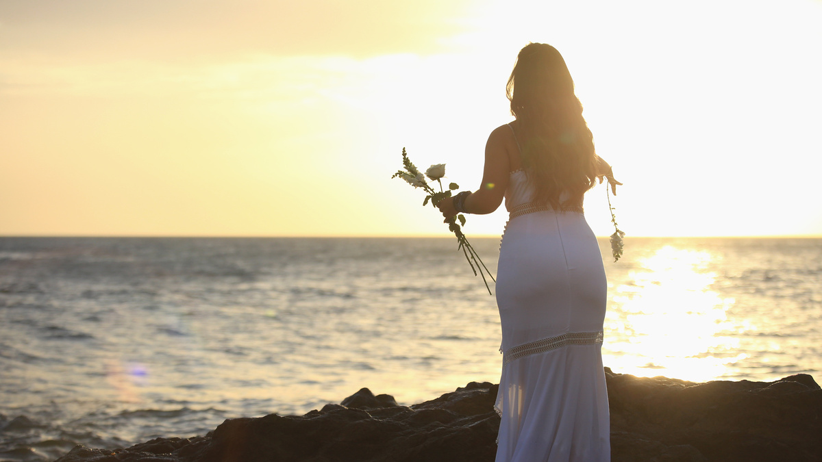 Mulher de Candomblé à beira do mar com flores.