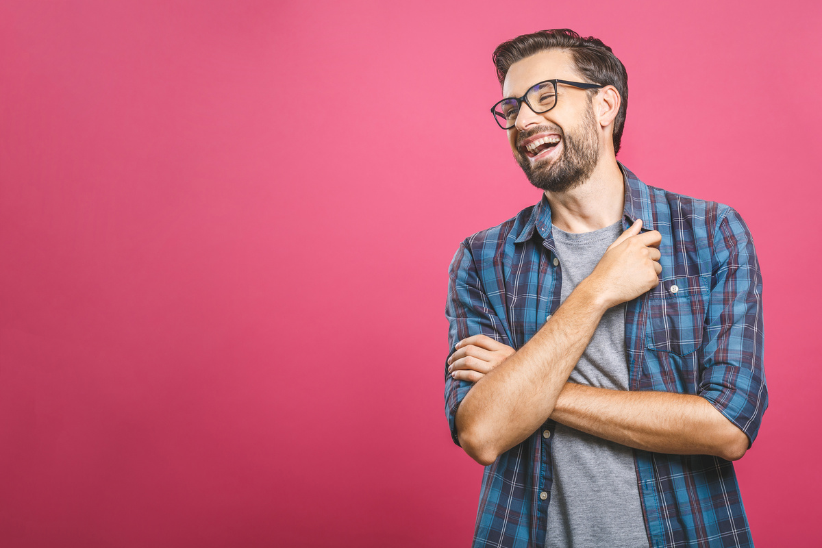 Homem vestindo camisa xadrez e óculos pretos enquanto ri sozinho, representando o comportamento bem humorado do homem de Gêmeos.