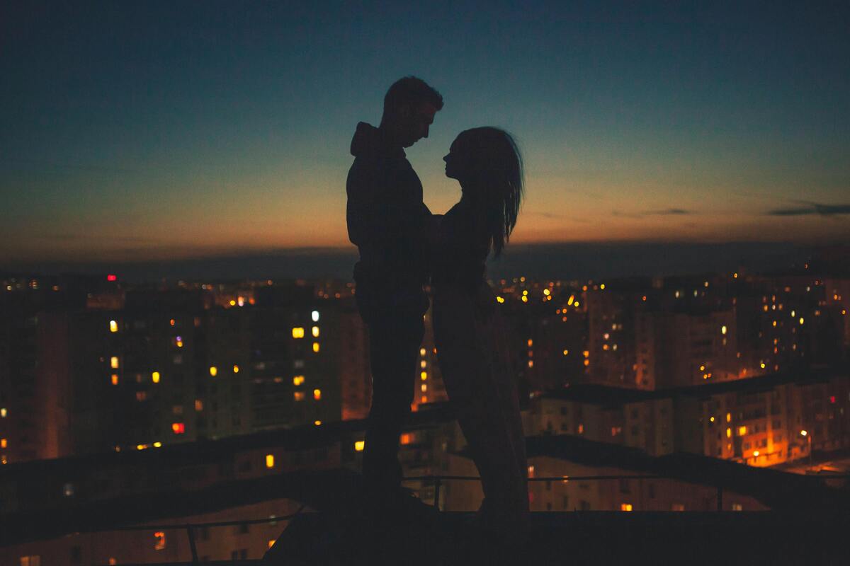 Silhueta de um casal em frente a uma cidade iluminada.