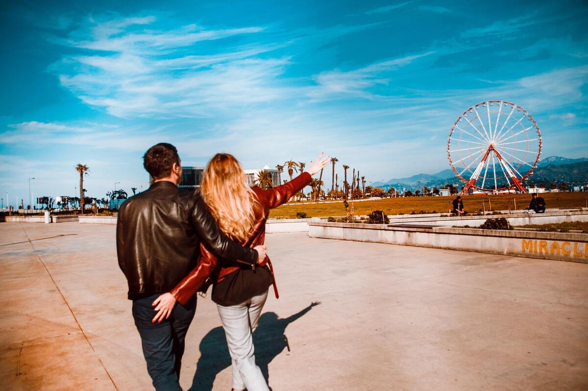 Casal abraçado observando um parque de diversões ao fundo.