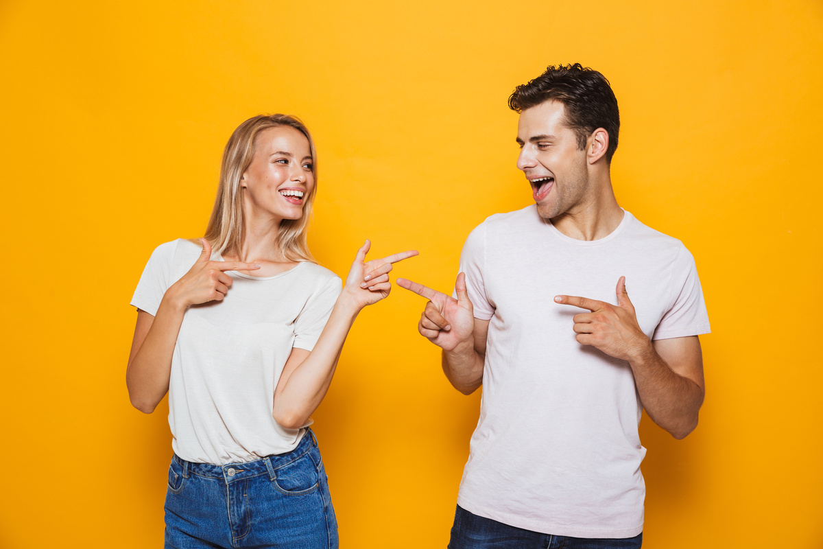 Mulher e homem posando um para o outro em meio a cenário amarelo, representando a interação de Áries e Leão com base no gênero.