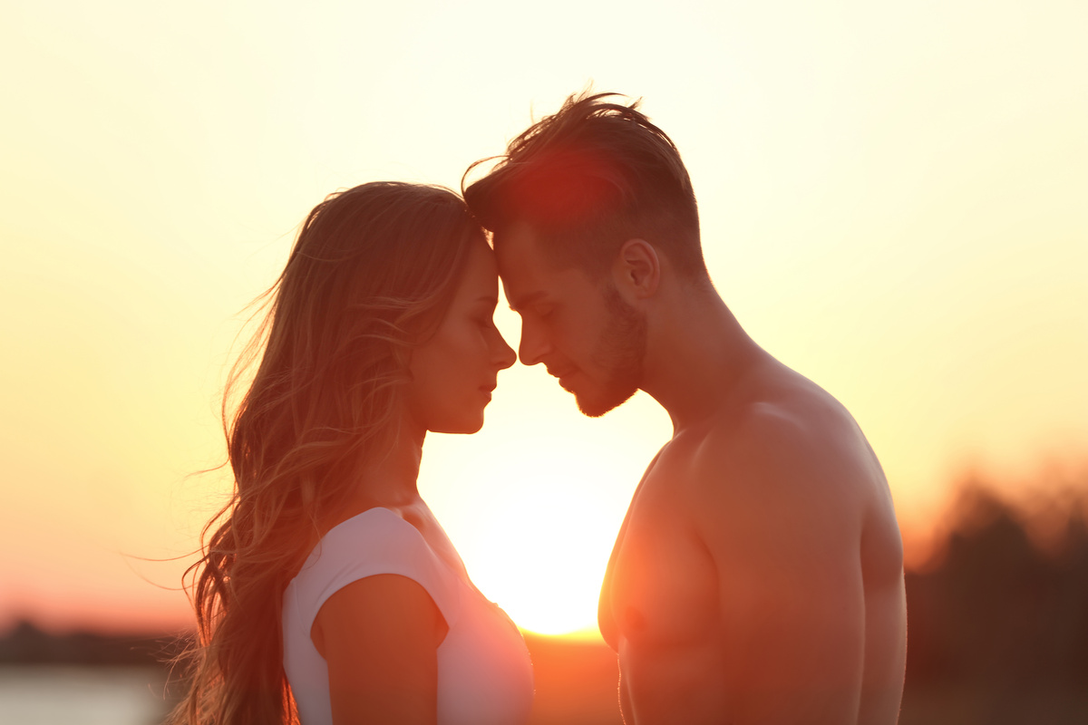 Mulher e homem com as testas juntas, em frente a por do sol, representando a combinação Áries e Leão.