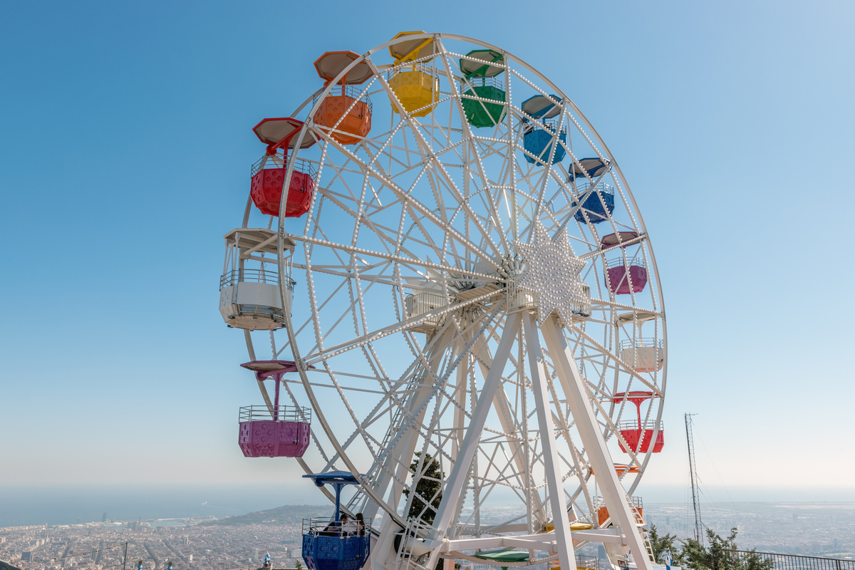 Roda gigante branca com cabines coloridas, em meio a céu azulado e aberto.