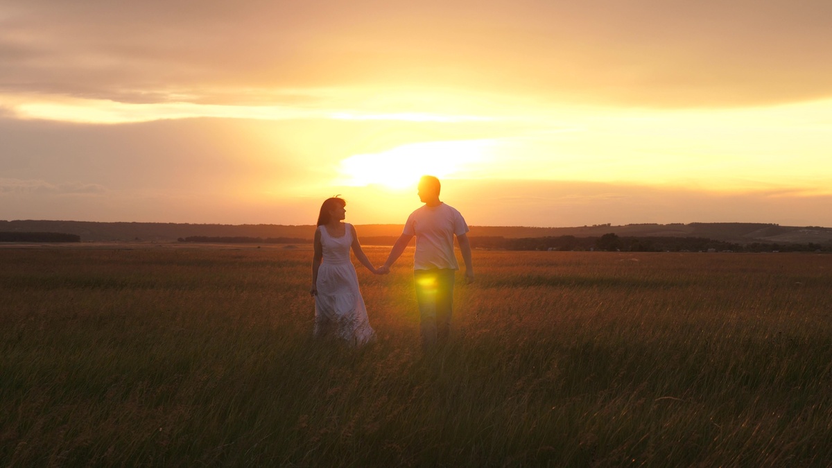 Casal andando de mãos dadas no pôr do Sol