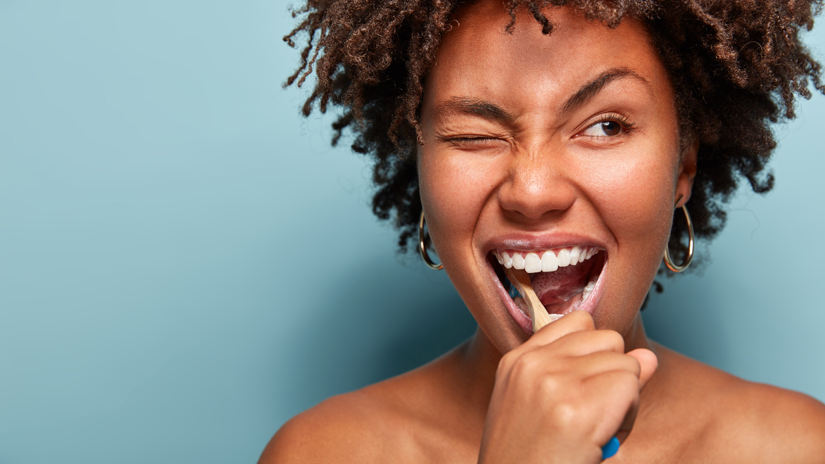 Mulher fazendo a higiene bucal com escova de dentes.