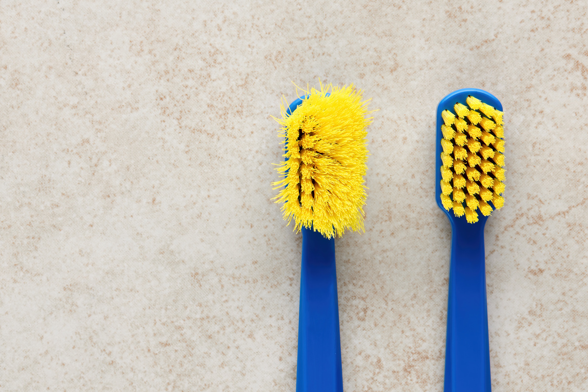 Duas escovas de dente. Ao lado esquerdo, uma velha e desgastada; ao direito, uma escova de dentes nova.