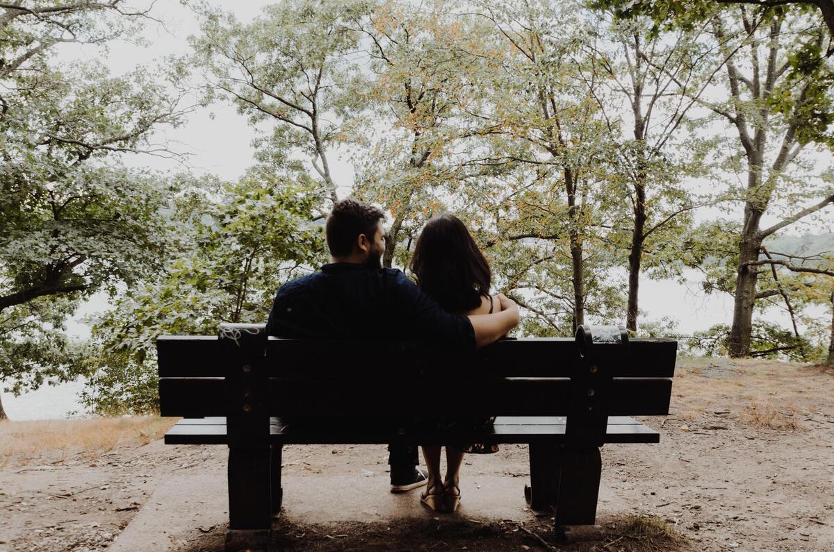 Casal sentado em banco de parque olhando a paisagem.