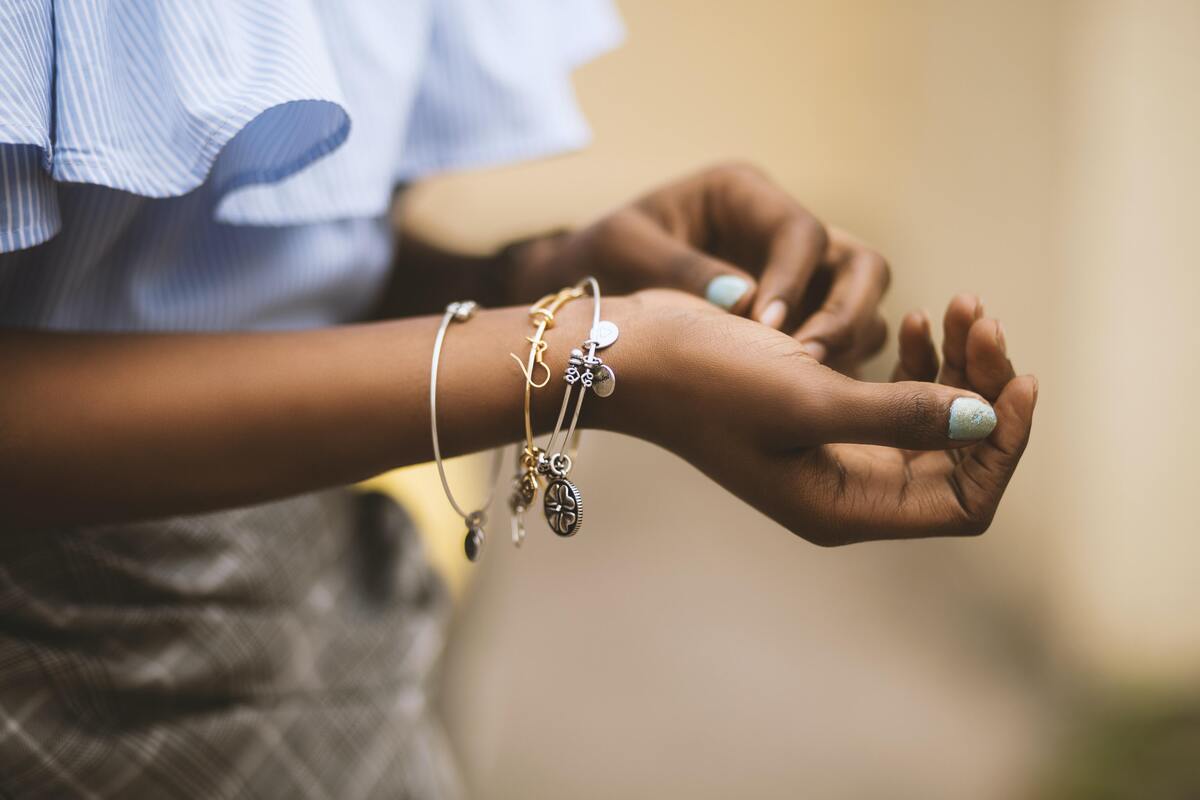 Pulso feminino com três pulseiras com pingentes: duas de prata e uma de ouro. 